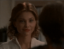 a woman in a white jacket looks at a man in a dark room with a candle in the background