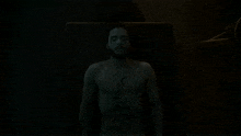a close up of a shirtless man with a beard making a funny face in the dark .