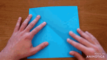 a person is folding a piece of blue paper .