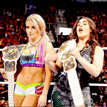 two female wrestlers are holding their championship belts in a wrestling ring with a crowd watching