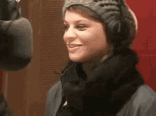 a woman wearing headphones and a scarf is smiling while standing in front of a microphone .