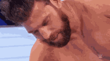 a shirtless man with a beard is laying down with a wrestling logo on his chest