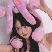 a woman is wearing a pink and purple stuffed rabbit on her head