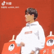 a man in a supreme hoodie is standing in front of a red wall .
