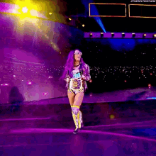 a woman with purple hair is walking on a stage with a microphone in her hand .