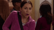 a woman in a purple jacket with hoop earrings looks surprised