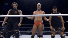 three men are standing in a wrestling ring with the word live on the screen