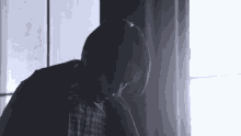 a man in a plaid shirt is sitting in front of a window looking down