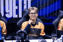 a man wearing glasses and a saigon phantom jersey sits in a chair