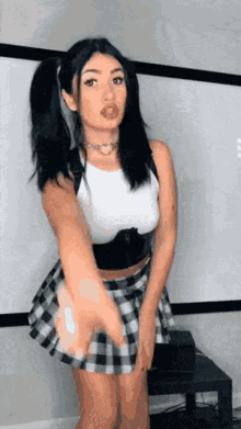 a woman in a plaid skirt and a white top is standing in front of a white board .