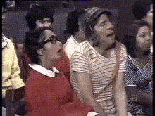 a group of people are sitting in a room and one of them is wearing glasses and a red sweater