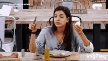 a woman is sitting at a table holding a knife and a piece of food .