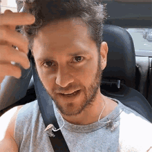 a man with a beard is sitting in the back seat of a car wearing ear buds .