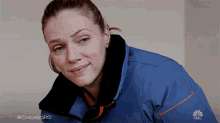 a woman wearing a blue jacket with the nbc logo on the front