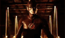 a man in a flash costume is standing in a dark room with lights behind him .
