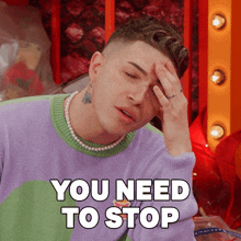 a man wearing a purple sweater and a pearl necklace holds his hand to his forehead and says you need to stop