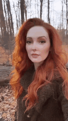 a woman with red hair is wearing a brown coat in the woods