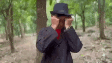 a man in a suit and hat is covering his eyes in the woods .
