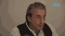a man in a white shirt and black vest is talking in front of a wall with the letters gzt on it