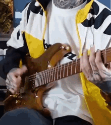a man with tattoos is playing a guitar while wearing a yellow and white jacket .