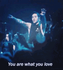 a man stands in front of a crowd with the words " you are what you love " above him
