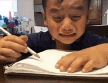 a young boy is crying while writing on a piece of paper with a pencil .