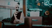 a clown is sitting at a table in front of a sign that says taco bell