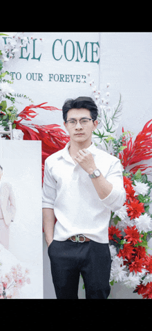 a man wearing glasses stands in front of a sign that says " welcome to our forever "