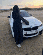a woman in a black abaya stands in front of a white bmw