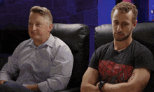 a man wearing a spider-man shirt sits next to another man