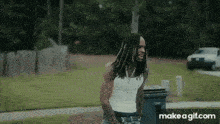 a man with dreadlocks is standing next to a trash can .
