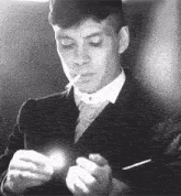 a black and white photo of a man in a suit and tie lighting a cigarette .