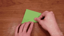 a person is holding a piece of green paper on a wooden table with the words made in animatica visible