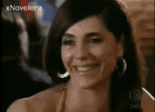 a woman is smiling and looking at the camera while wearing hoop earrings and a necklace .