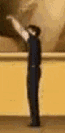 a man in a suit is standing in front of a yellow wall with his arm outstretched .