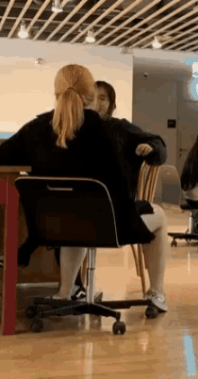 a woman is sitting in a chair with her legs crossed while another woman sits at a desk .