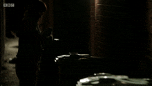 a woman is walking down a dark alleyway with bbc written on the bottom right