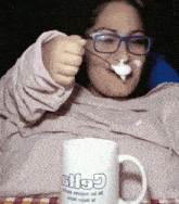 a woman with glasses is eating yogurt from a mug that says stl5