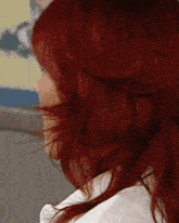 a woman with red hair is wearing a white shirt and has her hair blowing in the wind