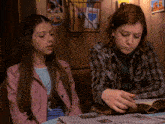 a girl in a pink jacket sits next to another girl who is reading a book