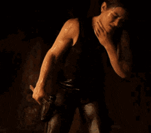a woman in a black tank top is holding a gun in her hand and covering her face with her hand .