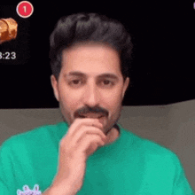 a man with a mustache is covering his mouth with his hand while wearing a green shirt .