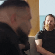 a man with a beard is sitting next to another man in a black shirt