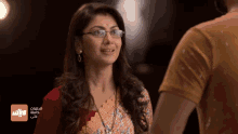 a woman wearing glasses stands next to a man in a yellow shirt with arabic writing on it