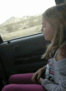 a young girl is sitting in the back seat of a car looking out the window