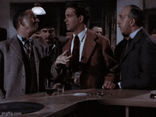 a group of men are standing around a bar talking to each other and one of them is smoking a cigarette .