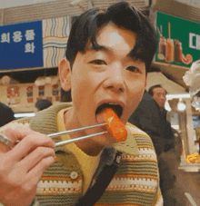 a man is eating a sausage with chopsticks in front of a sign that says ' a ' on it
