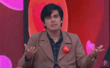 a man in a brown jacket and plaid shirt is sitting in front of a red screen .