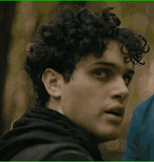 a young man with curly hair is wearing a black hoodie and looking at something .