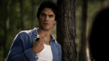 a man in a blue shirt is leaning against a tree looking at something